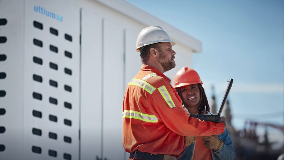 A close-up of two electricians stand in front of an Ultium stationary energy storage vault talking to each other.