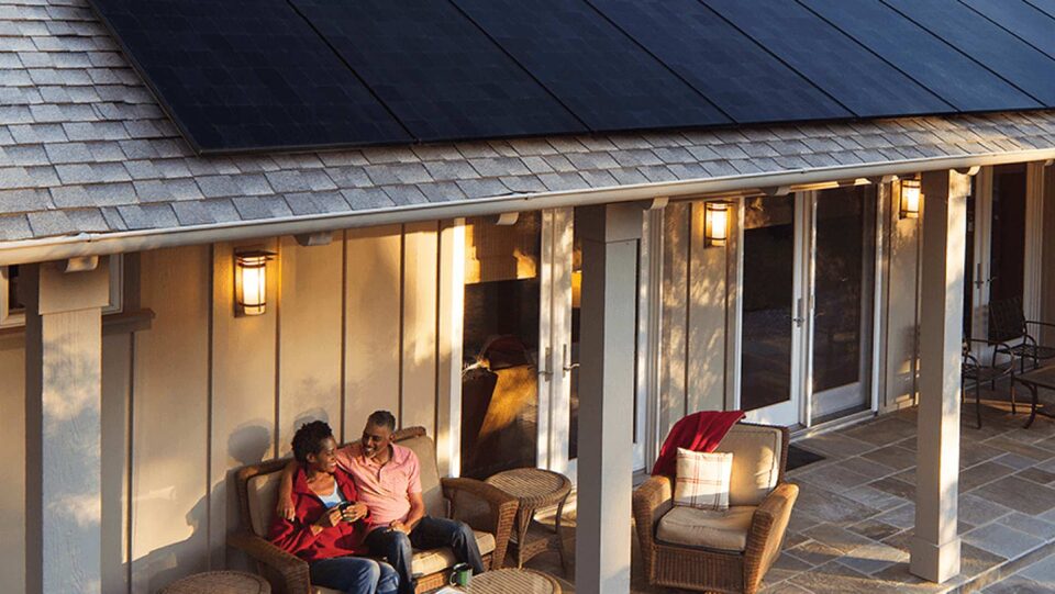 A couple sits on their back deck enjoying their morning coffee; also in view are the solar panels on their roof.