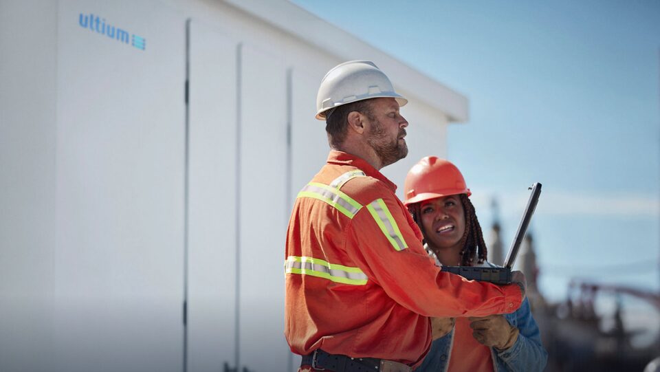 A close-up of two electricians stand in front of an Ultium stationary energy storage vault talking to each other.