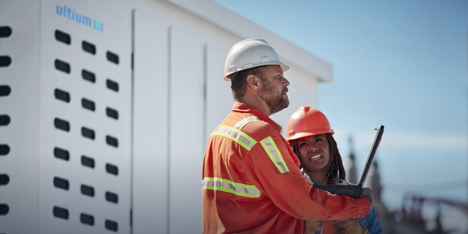 A close-up of two electricians standing in front of an Ultium stationary energy storage vault talking to each other.