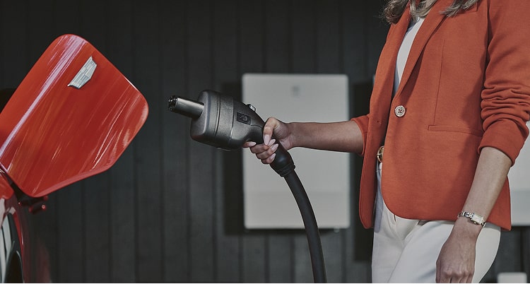 Person in red jacket plugging charger into EV in garage