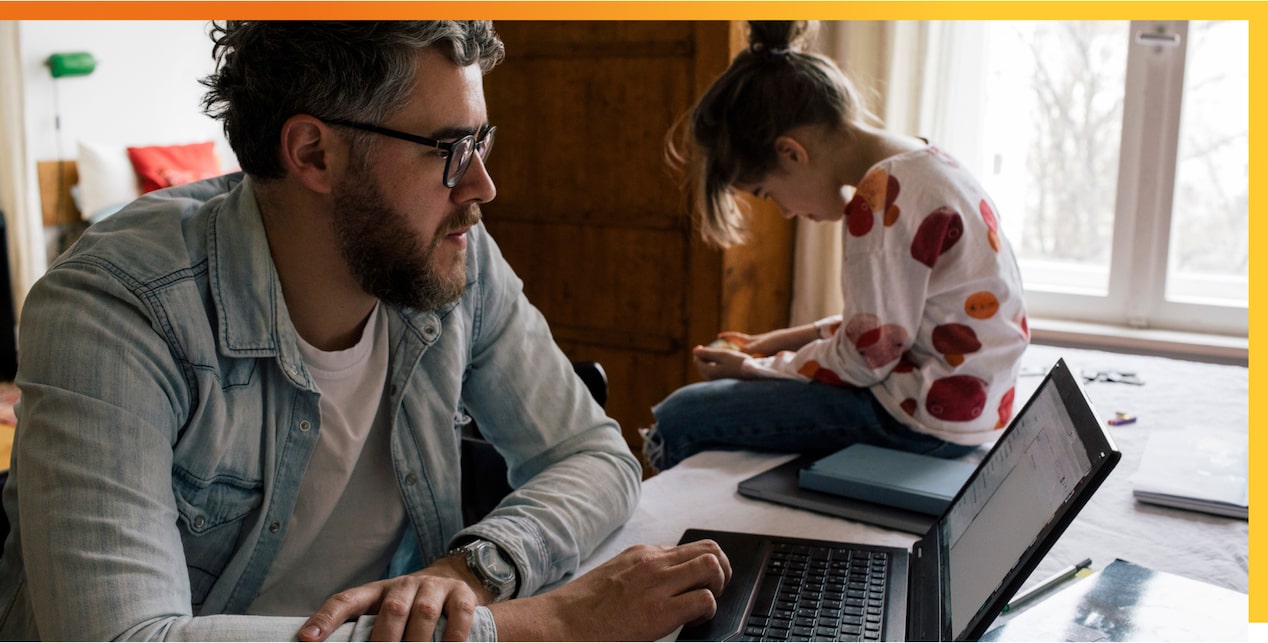 Man looking at laptop with little girt sitting on table next to him
