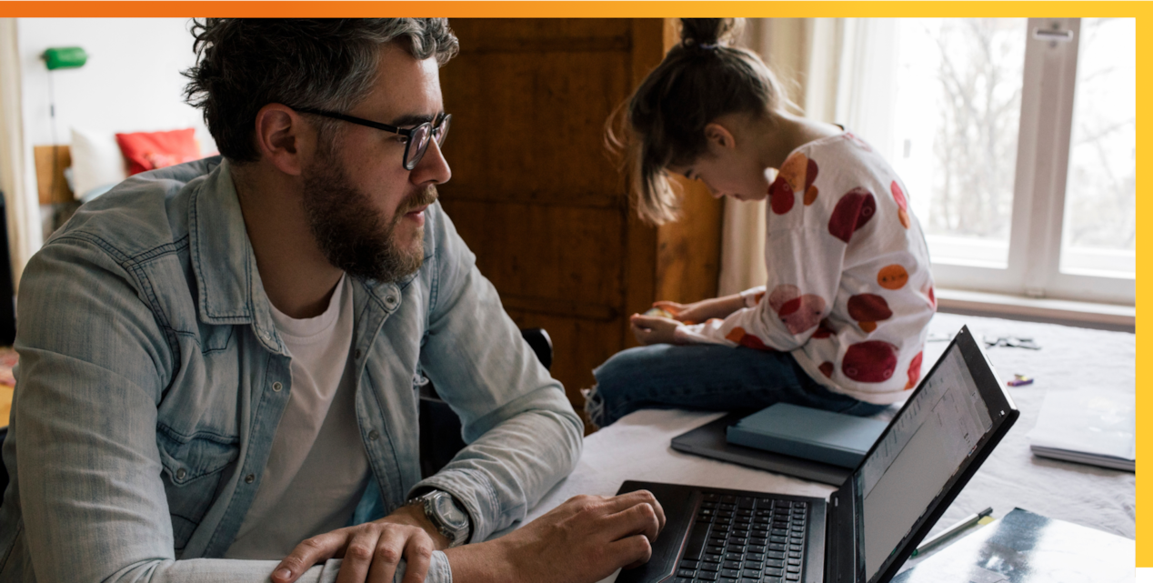 Man looking at laptop with little girt sitting on table next to him